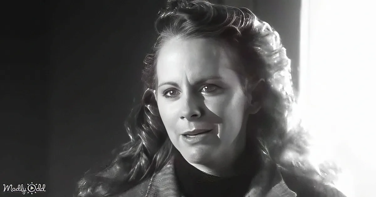 A woman with curly hair, wearing a dark turtleneck, gazes intently, set against a stark black and white background.
