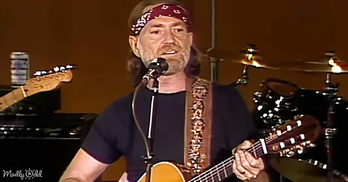 A man with a bandana sings into a microphone while playing an acoustic guitar.
