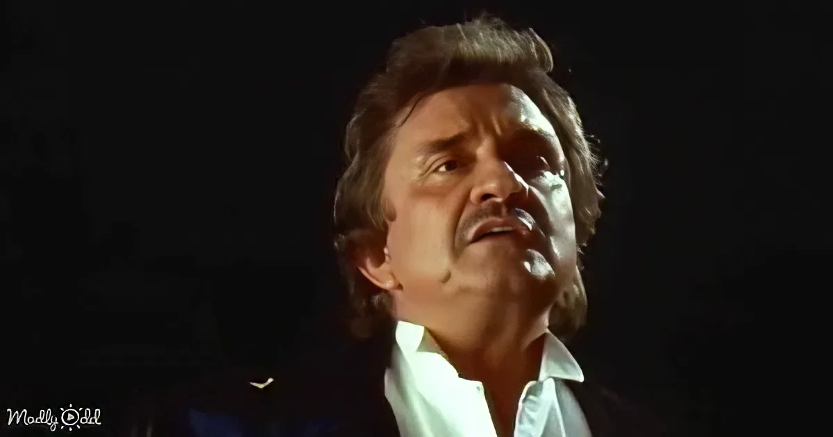 A man with long hair and a white shirt is looking upwards against a dark background.