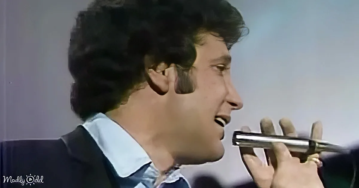 A man with curly hair in a suit is singing into a microphone.