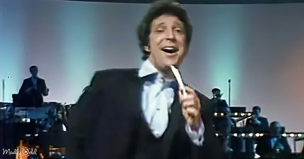 A man in a tuxedo sings passionately, holding a microphone, with a band in the background.