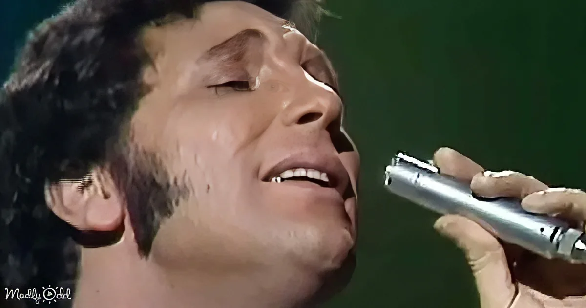 A man with dark hair and a microphone, singing passionately with his eyes closed.