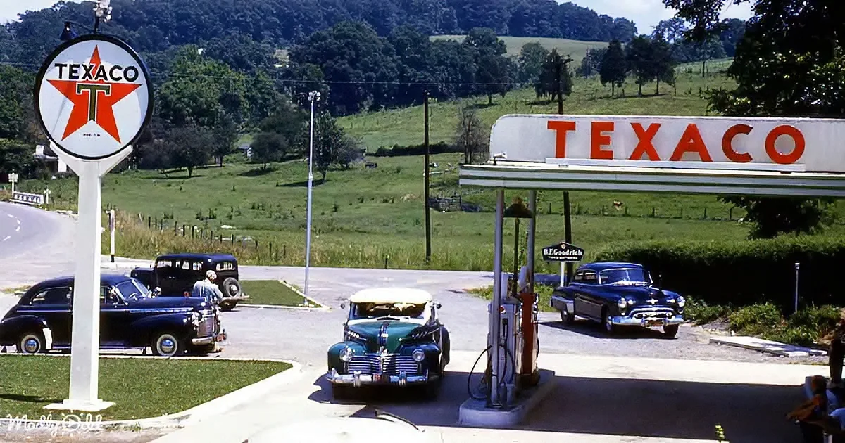 A vintage Texaco gas station with classic cars and a rural backdrop.