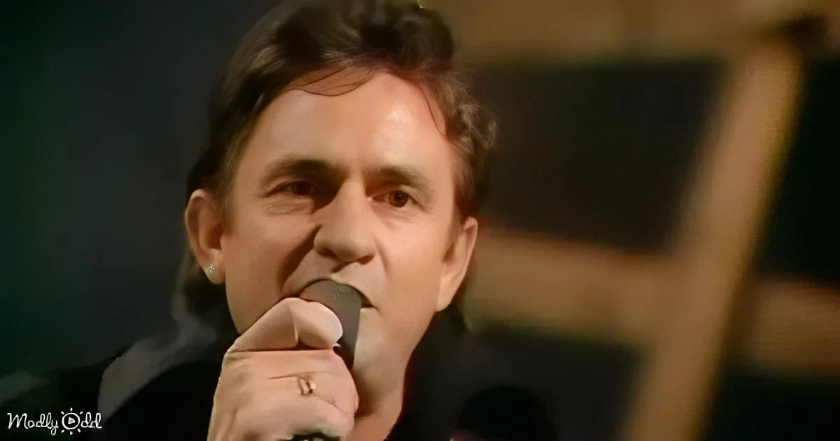 A person singing into a microphone, wearing a ring, with a blurred background.