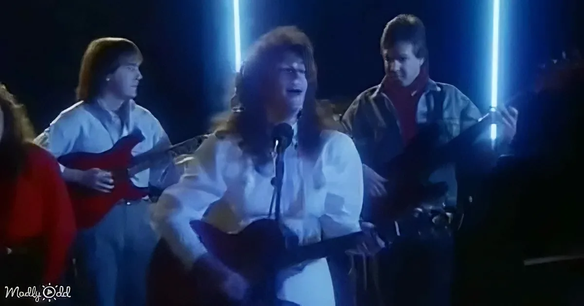 A person in white plays guitar on stage with a microphone, surrounded by other musicians.