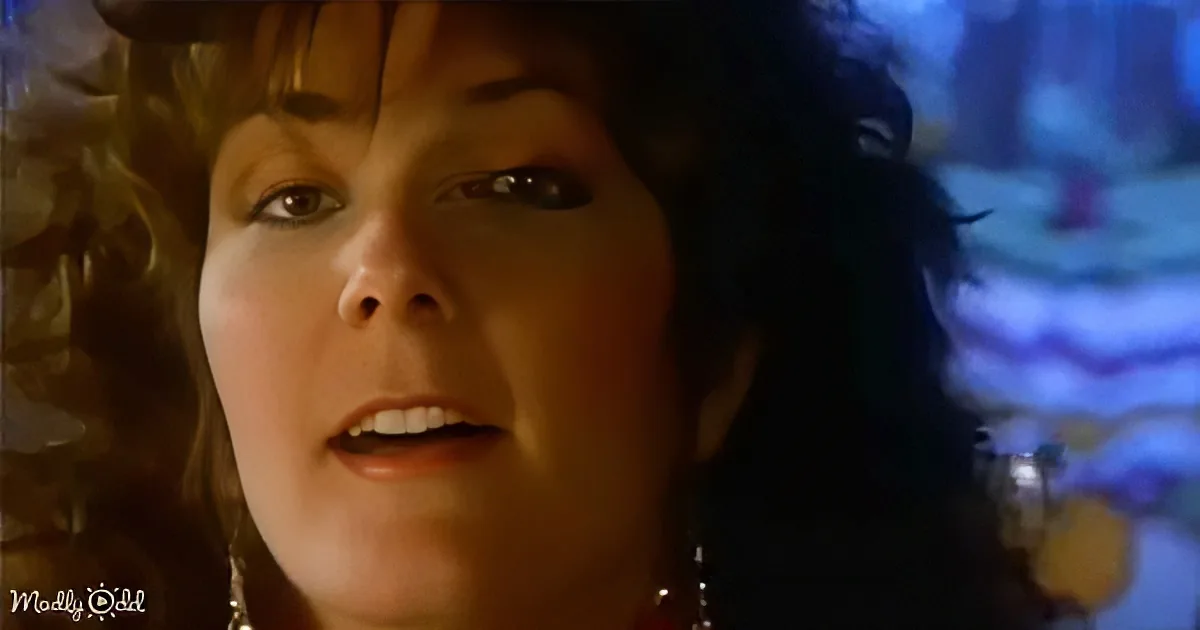 A woman with curly hair and earrings looks upward, mouth slightly open, in a dimly lit setting.