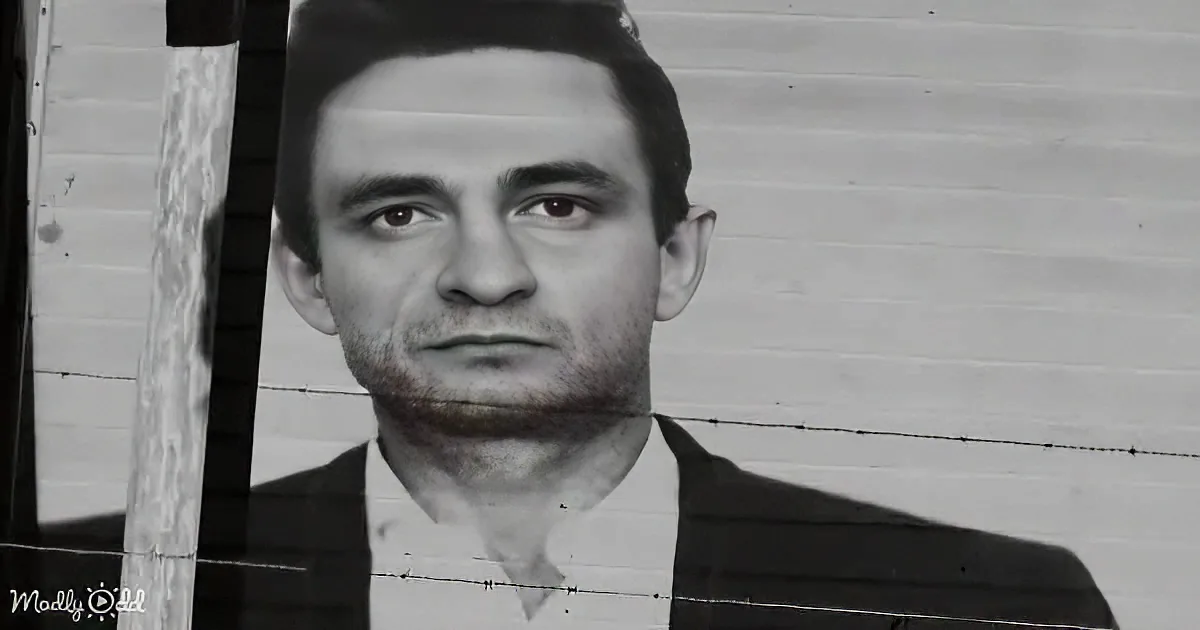 A man in a suit and tie is partially obscured by barbed wire against a brick wall.