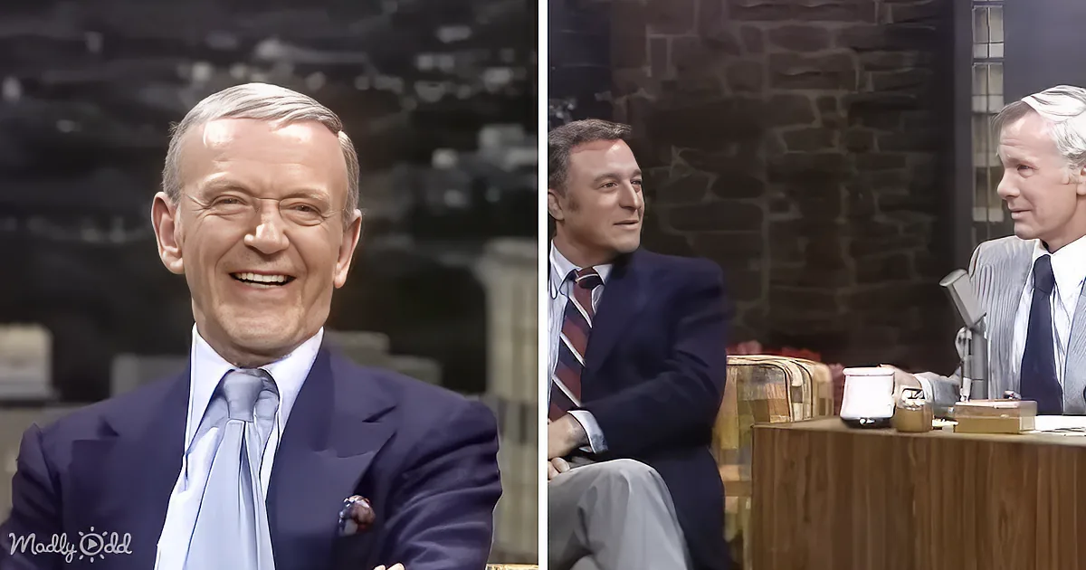 A man in a suit and tie smiles warmly, seated with others in a studio setting.