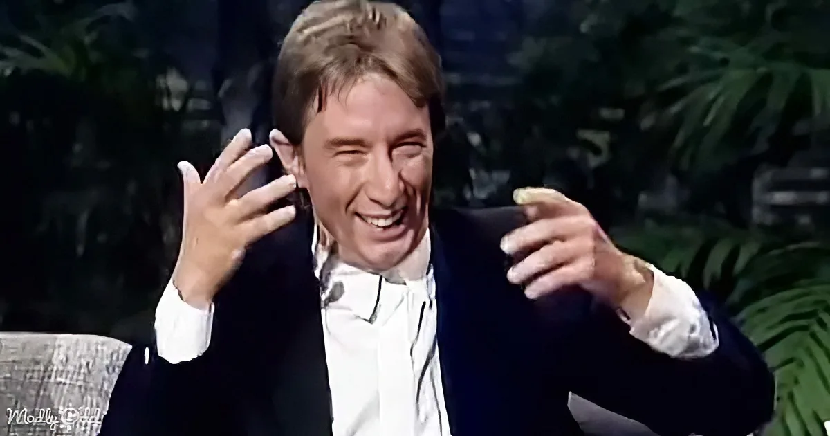 A man in a suit is laughing heartily, gesturing with his hands, and appears to be enjoying a humorous moment.