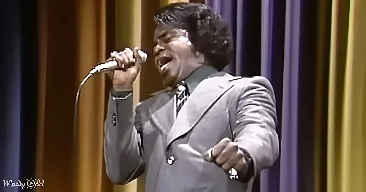 A man in a suit sings passionately into a microphone on stage.