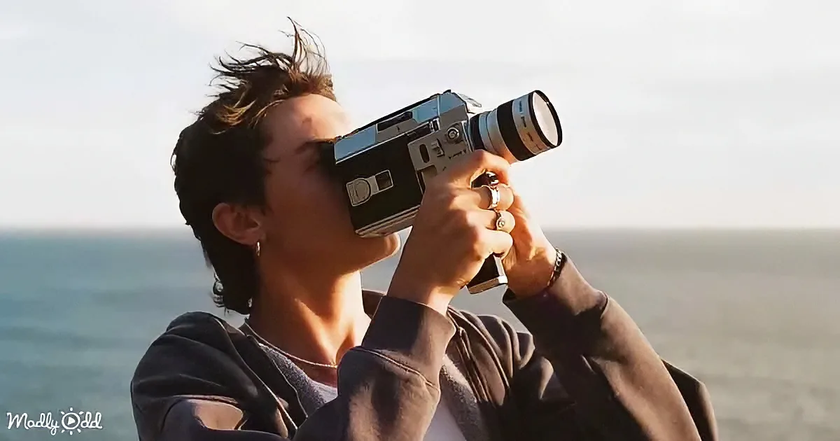 A person holding a vintage camera up to their face, capturing a scenic view of the ocean.