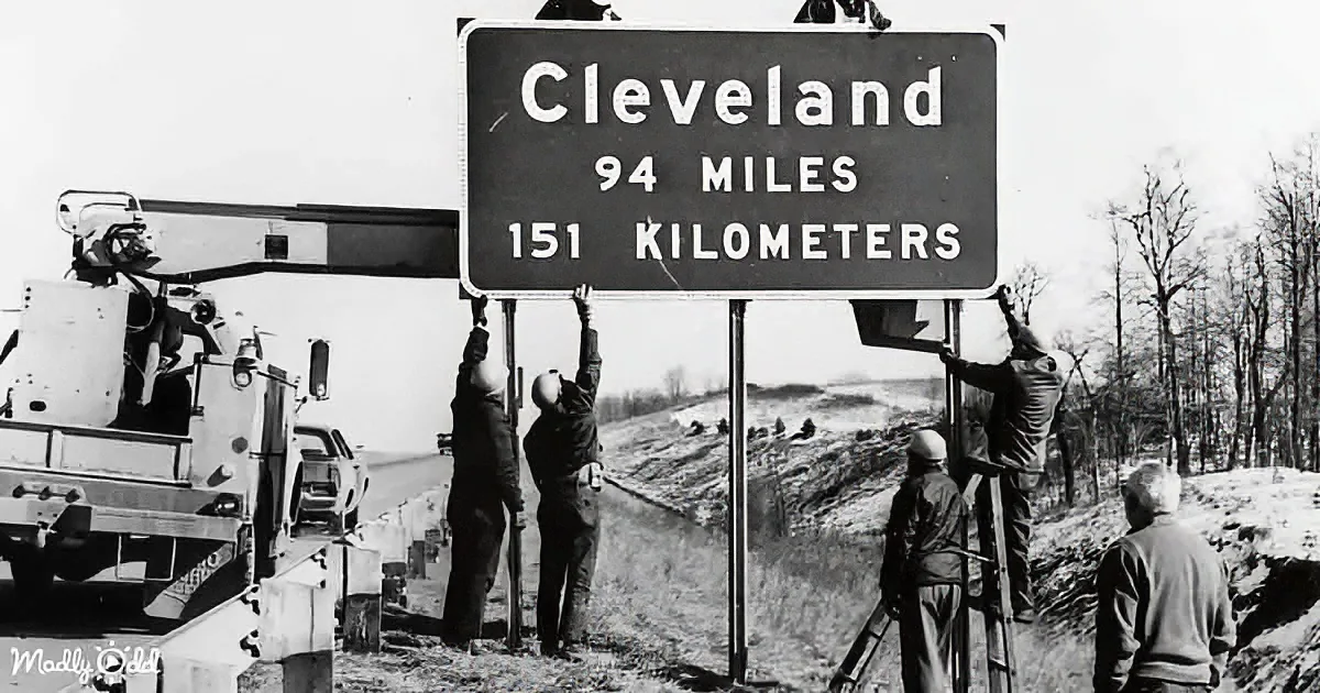 Workers install a sign indicating distance to Cleveland in miles and kilometers.