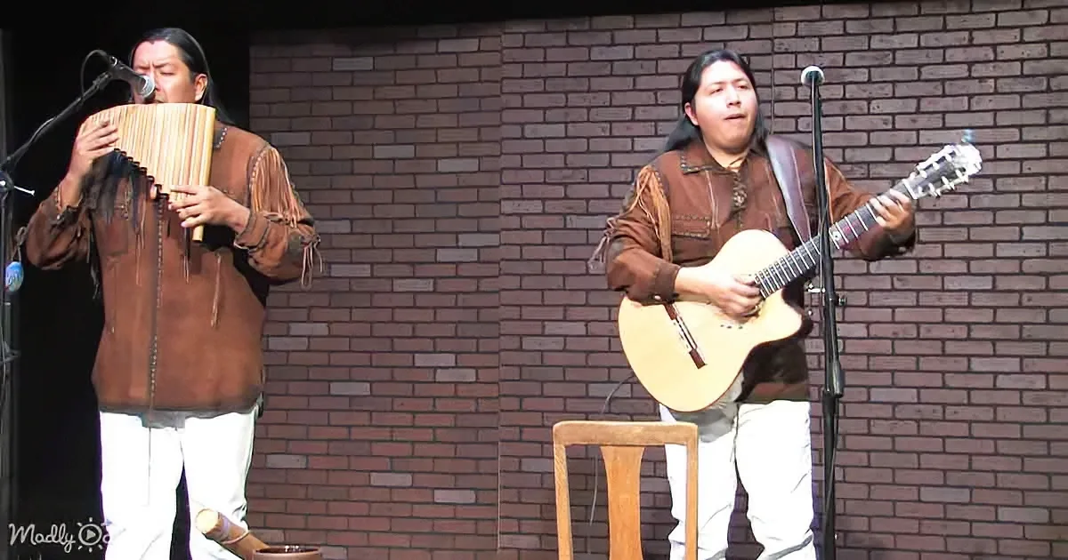Two musicians perform on stage, one playing a pan flute and the other a guitar.
