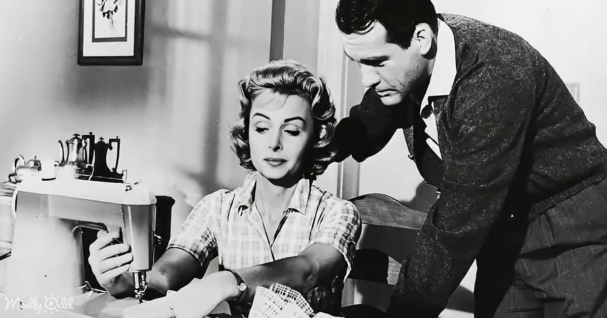 A woman sits at a sewing machine, focused, while a man leans in, observing her work.