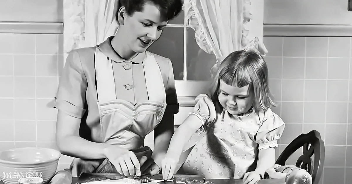 A woman and a young girl are cooking together in a kitchen, smiling and focused.