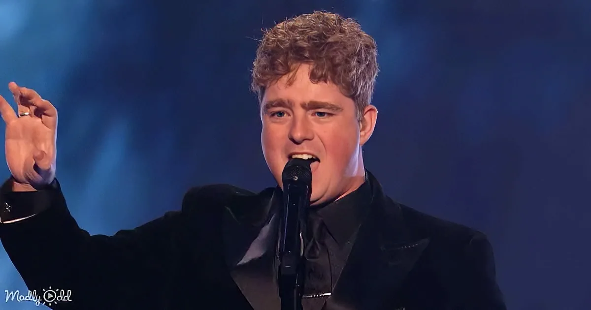 A man in a black suit sings passionately into a microphone, raising his hand in a gesture.
