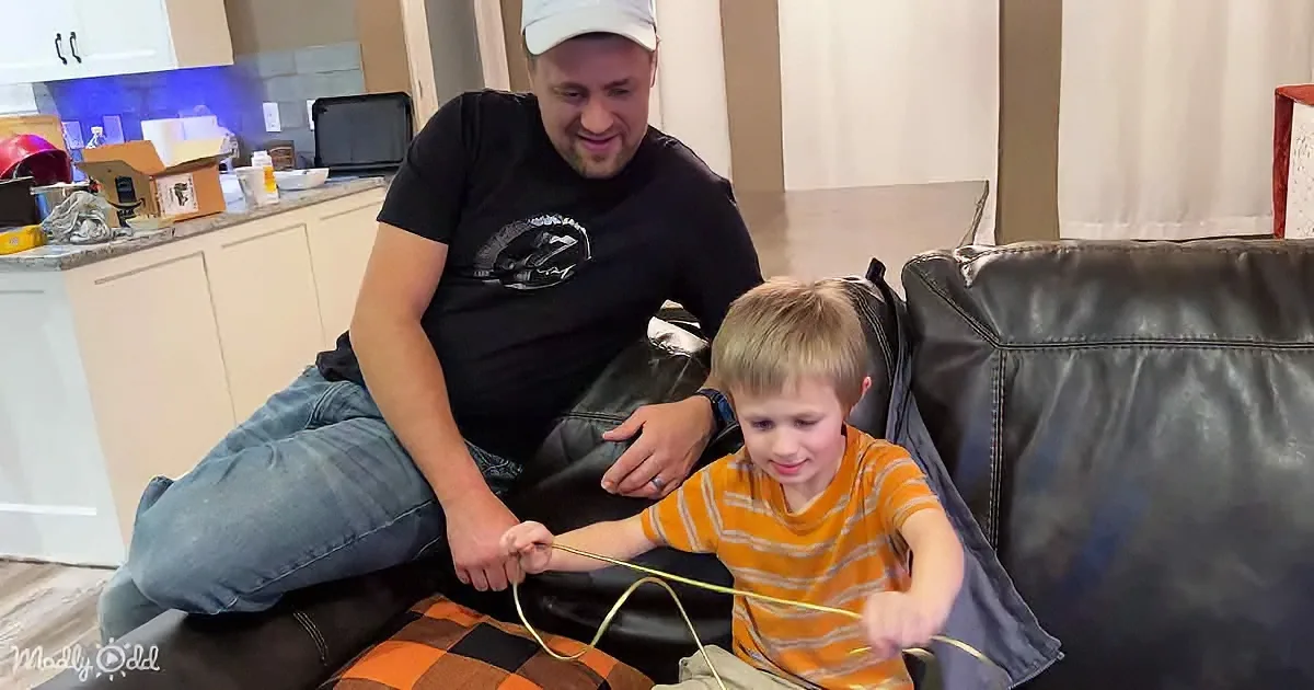 A man and a boy sit on a couch, the boy holding a yellow cord while the man watches.