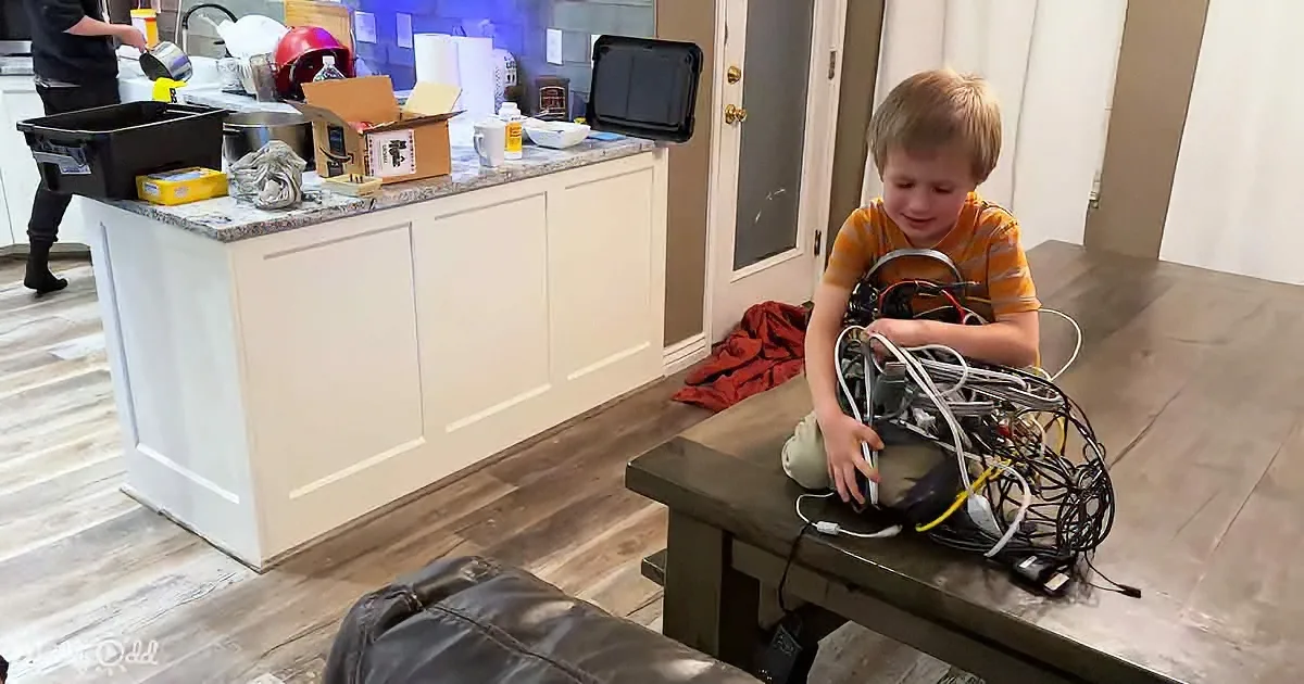 A young boy sits on a bench, holding a tangled mess of wires and cables.