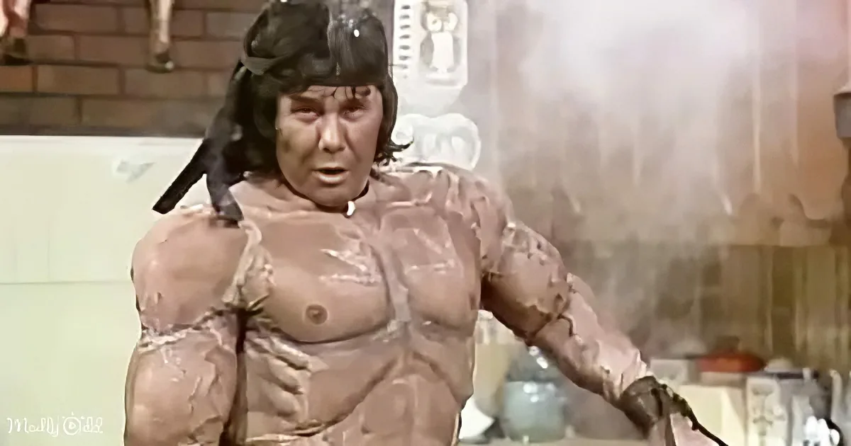 A muscular man with a bird perched on his head, covered in a brown substance, appears to be in a dramatic or comedic scene.
