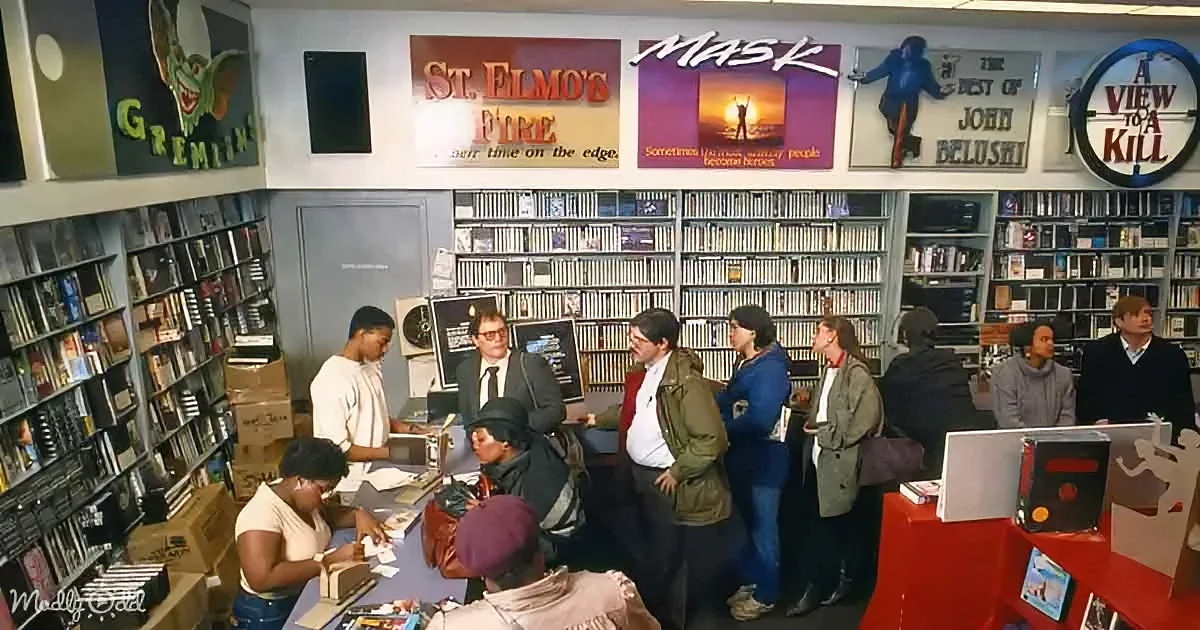 People gather in a bustling video store filled with movie posters and shelves of tapes.