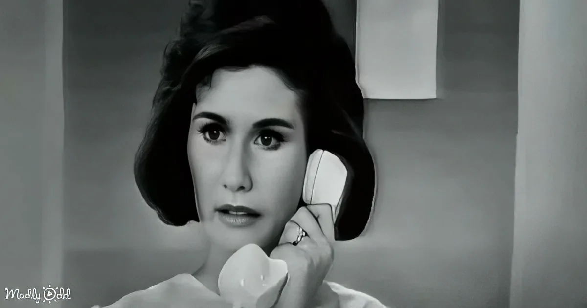 A woman with dark hair, wearing a ring, holds a white telephone receiver to her ear.