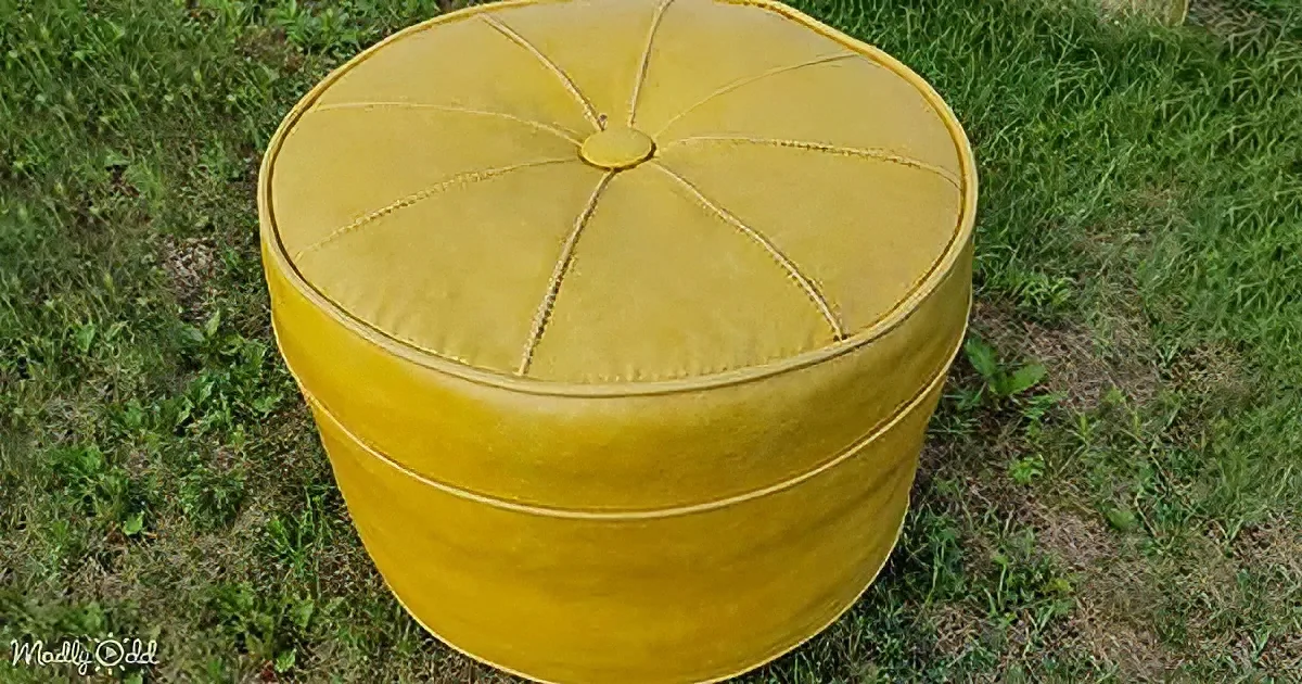 A mustard-yellow, round ottoman with a textured surface sits on grass.