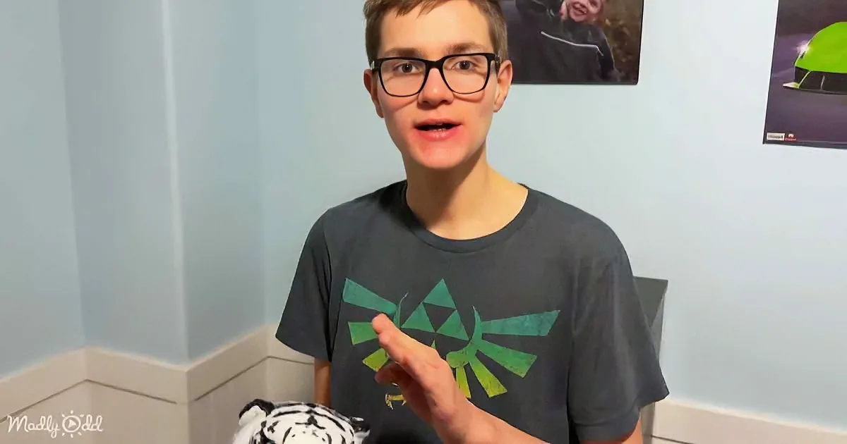A boy in a blue shirt sits on a bed with a stuffed dog, a book, and a hot water bottle.