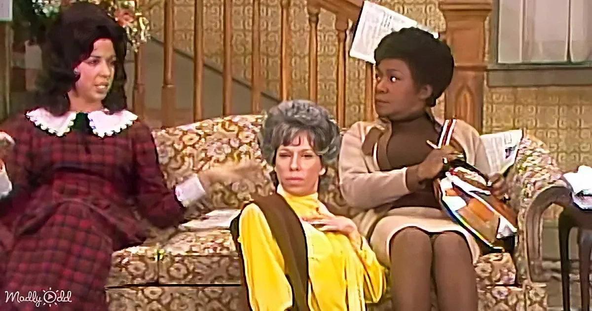 A woman in a yellow top sits on a floral-patterned couch, flanked by two others, in a vintage living room setting.