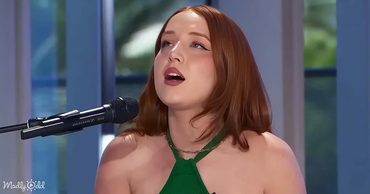 A woman with red hair and a green dress sings into a microphone, her eyes closed.