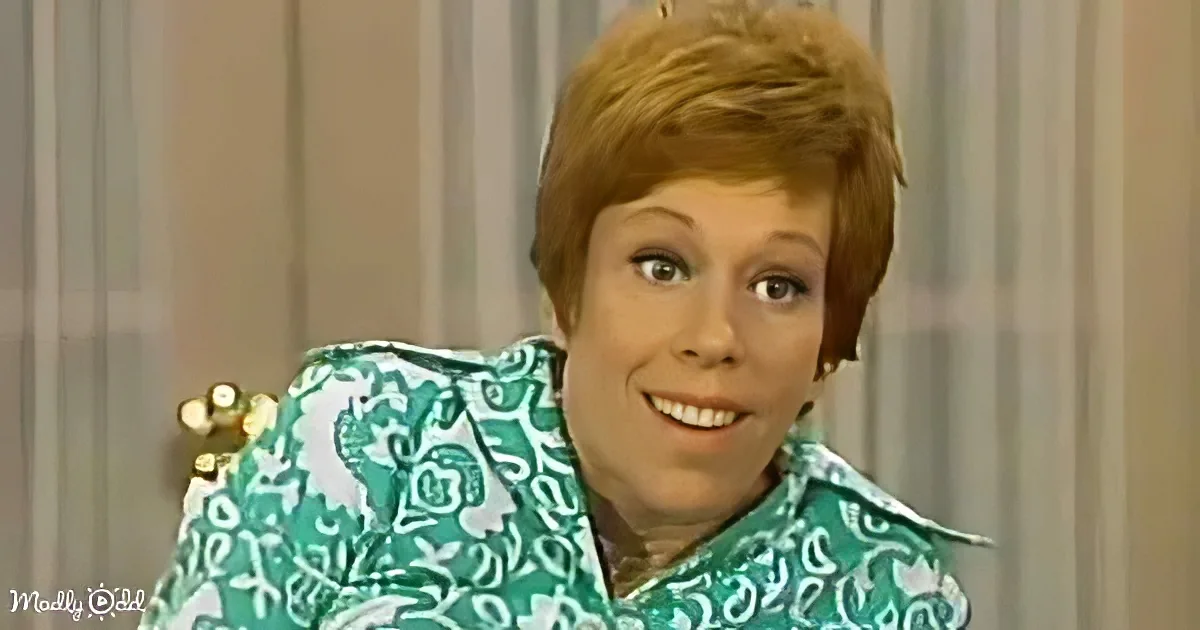 A woman with short red hair smiles, wearing a green patterned shirt, seated in a chair.