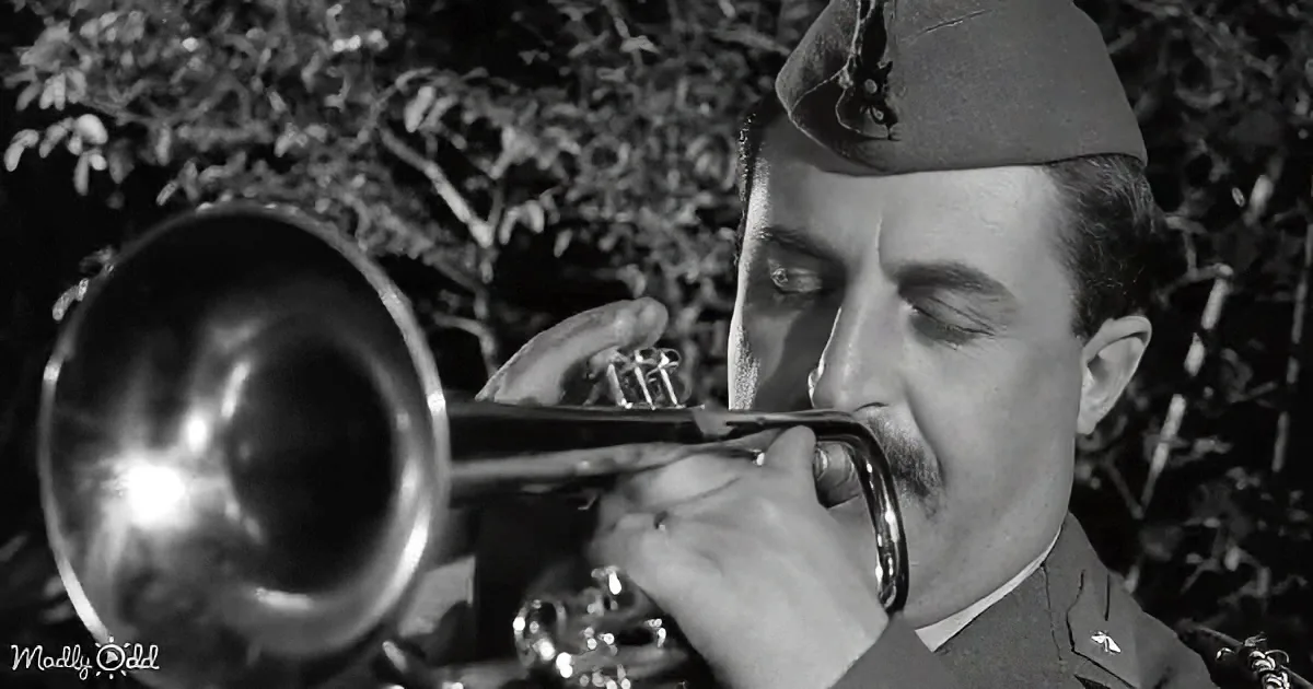 A man in a military uniform plays a trumpet with his eyes closed, surrounded by foliage.