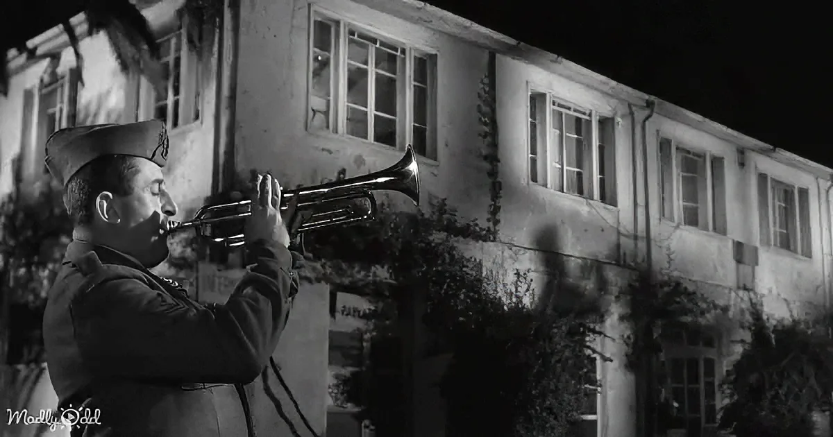 A man in a uniform plays a trumpet in front of a dimly lit building at night.