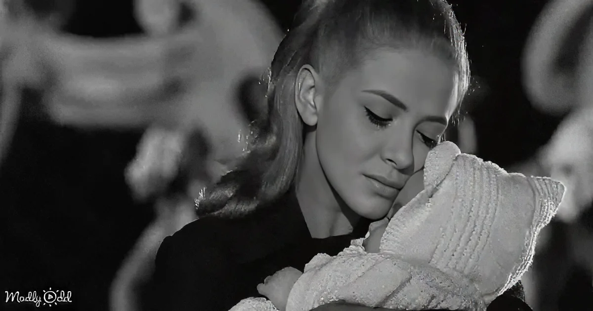 A woman cradles a baby, both in soft light, with blurred figures in the background.