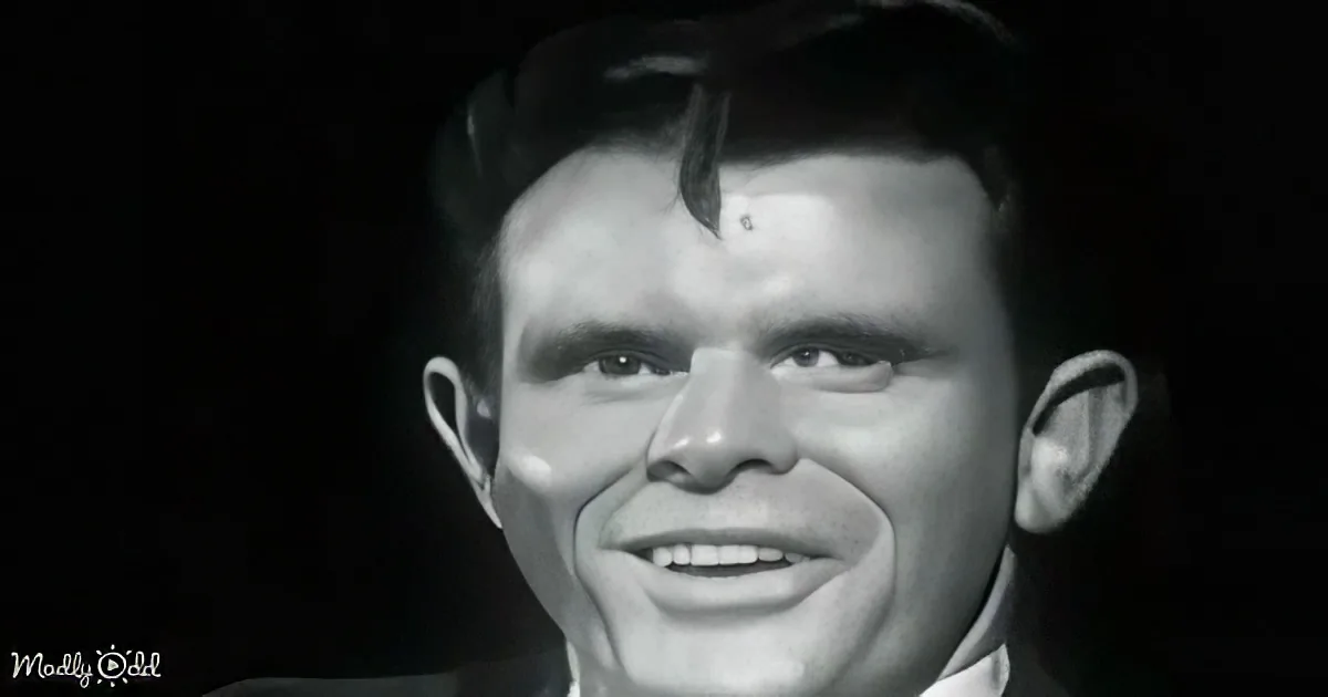 A man with a serious expression, wearing a dark suit, against a dark background.
