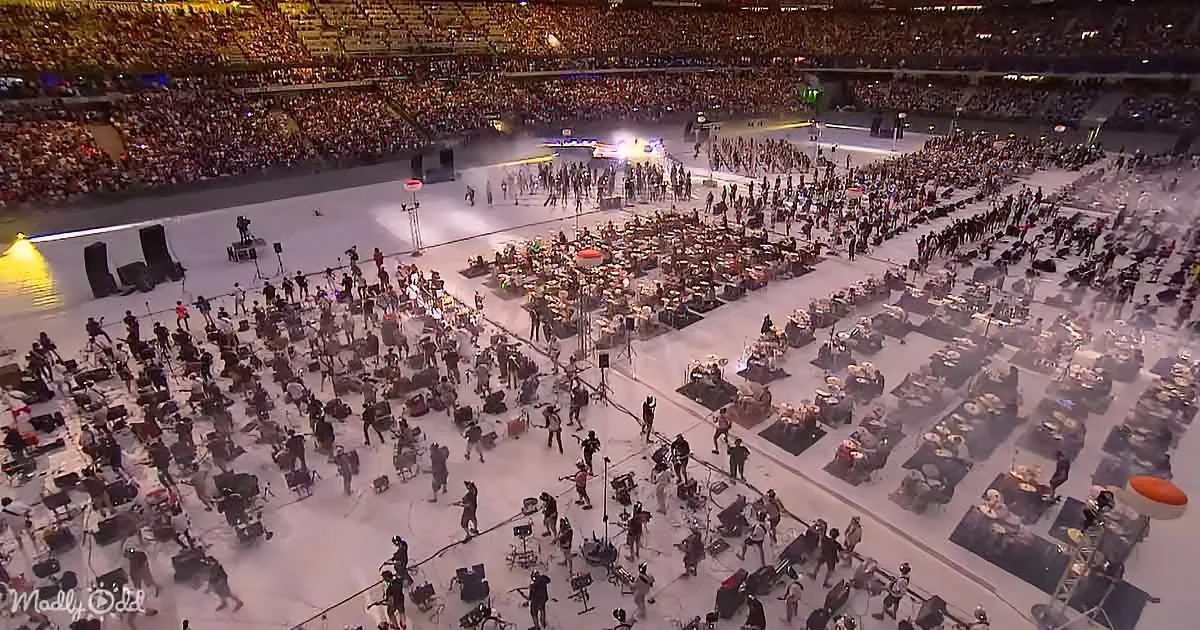 A massive concert stage with performers and a large audience in a packed arena.