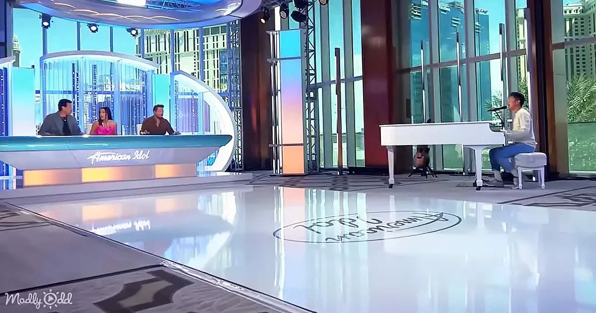 A pianist sits at a white piano on a shiny floor, with judges on a stage in the background.