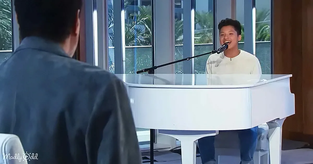 A young person sings into a microphone at a white piano, with another person seated nearby.