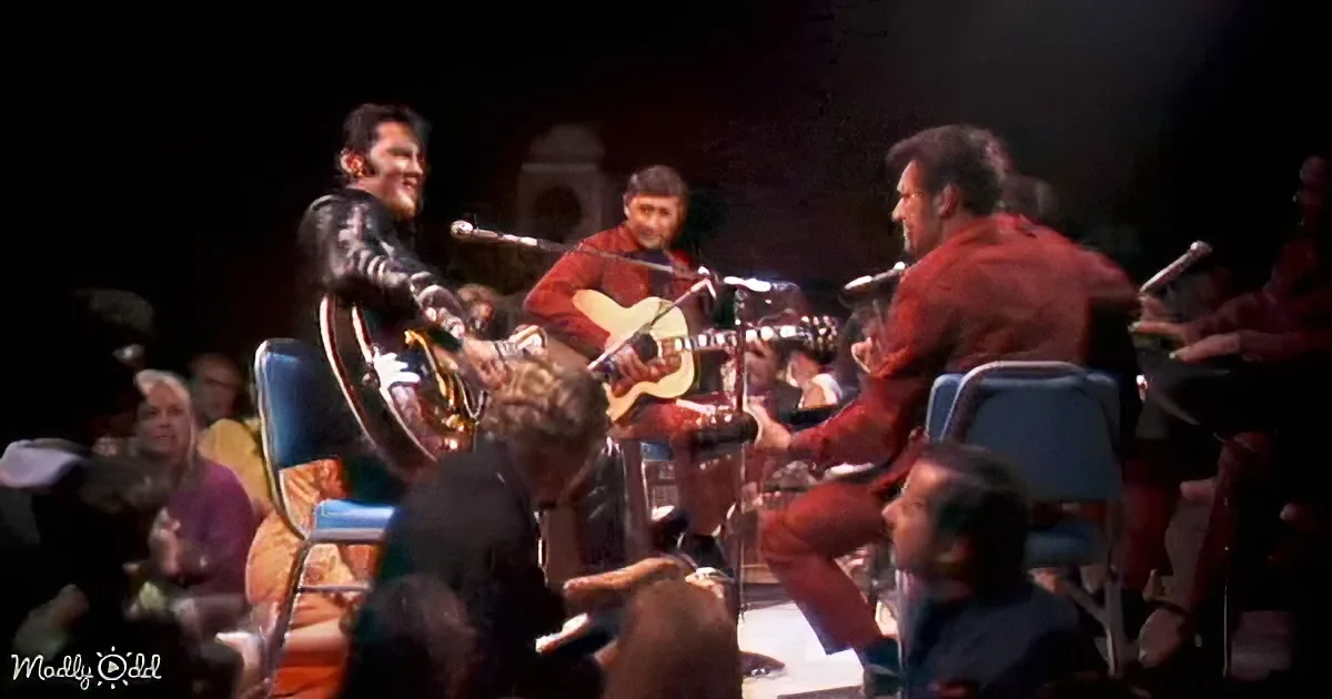 Elvis Presley plays guitar on stage with a band and audience in the background.