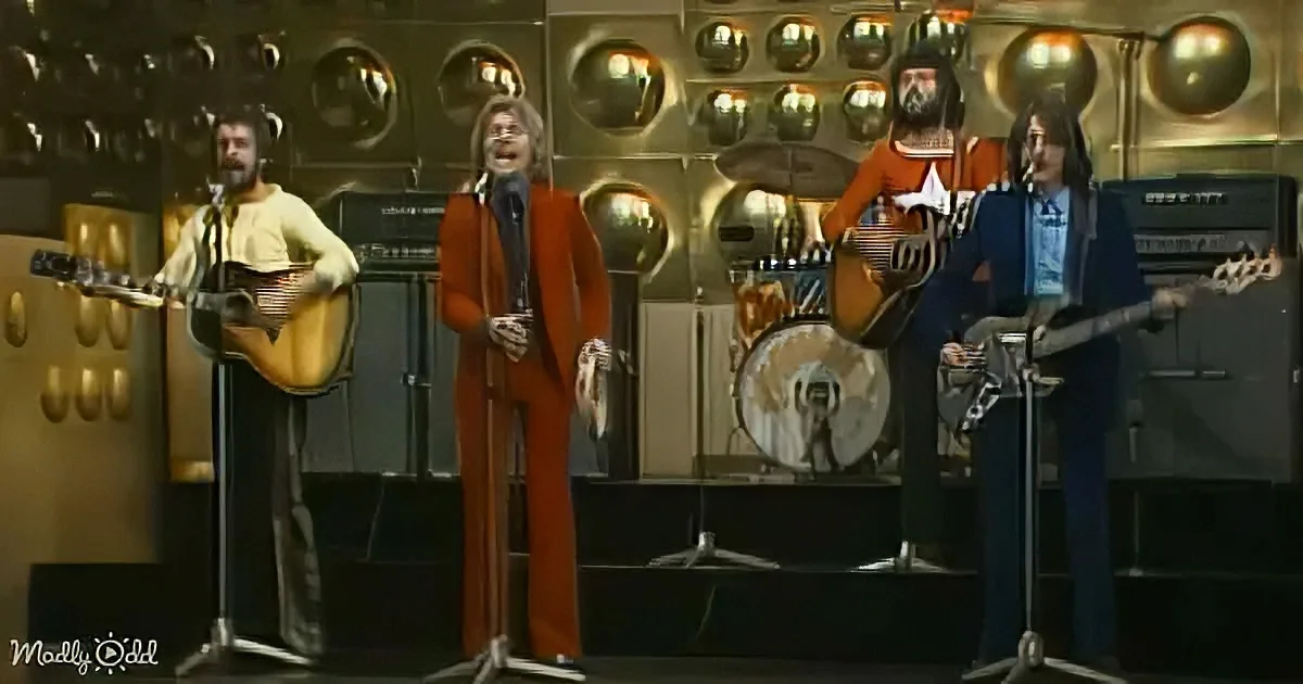 A man in a red suit sings into a microphone, accompanied by musicians with guitars and a bass.