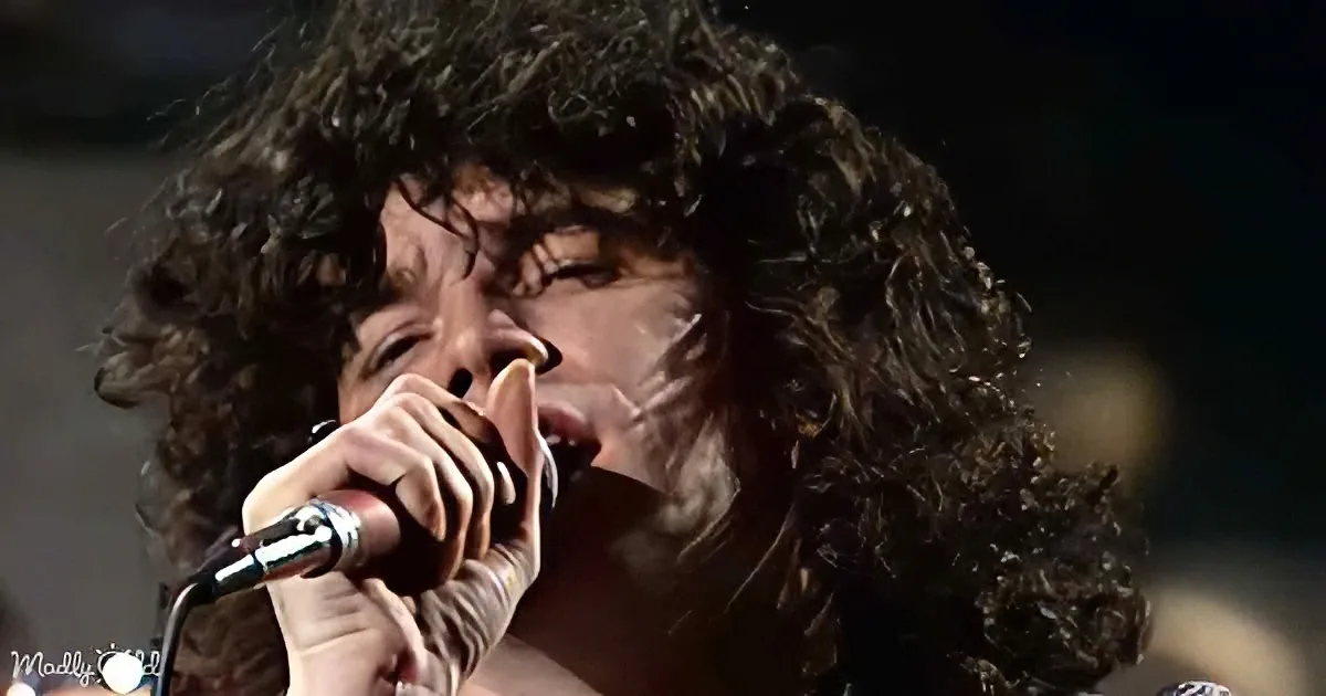 A person with curly hair is passionately singing into a microphone.