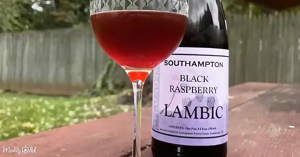 A glass of red lambic beer and its bottle are displayed on a table outside.