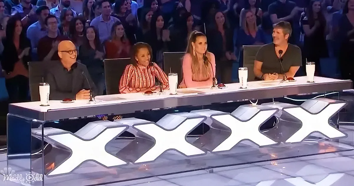 Judges seated at a table with "XXX" logo, audience in the background, drinks on the table.
