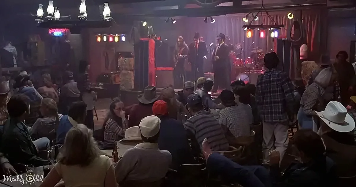 A band performs on stage in a dimly lit bar, surrounded by an audience in cowboy hats and casual attire.