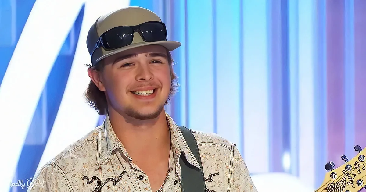 A smiling young man wearing a hat, sunglasses, and a floral shirt, holding a guitar.