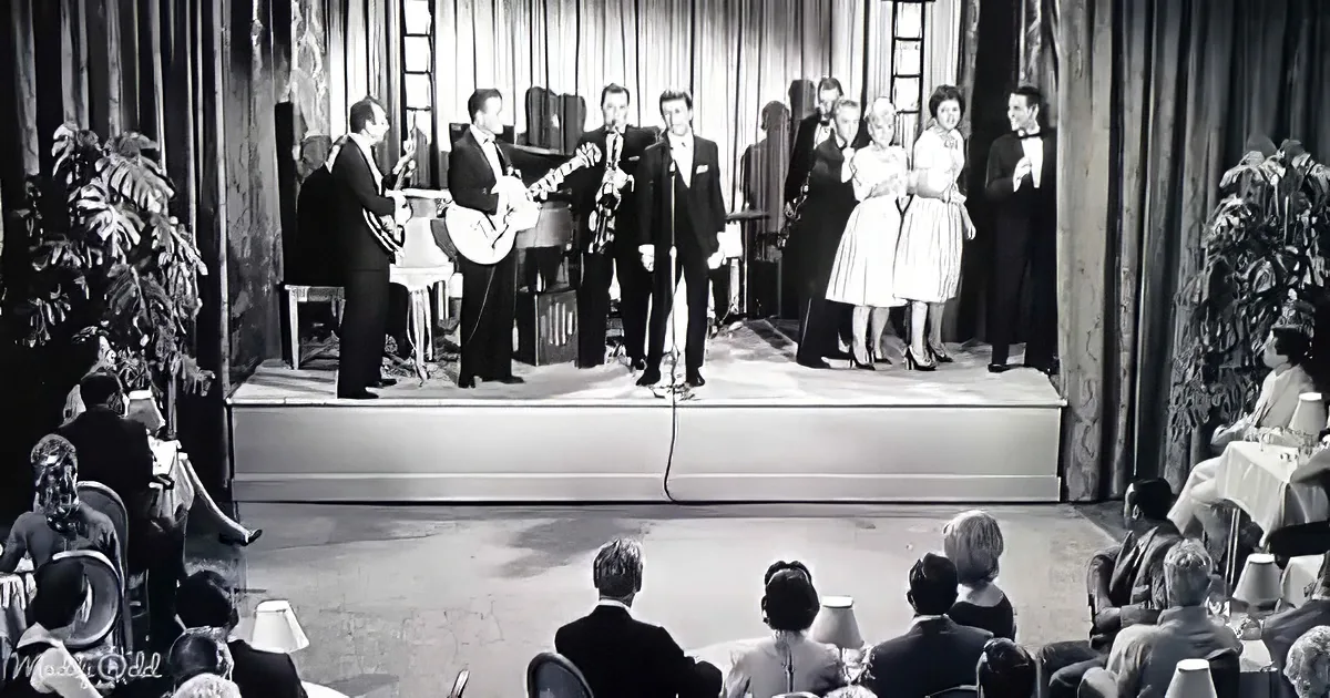 A band and singers perform on stage in front of an audience in a formal setting.