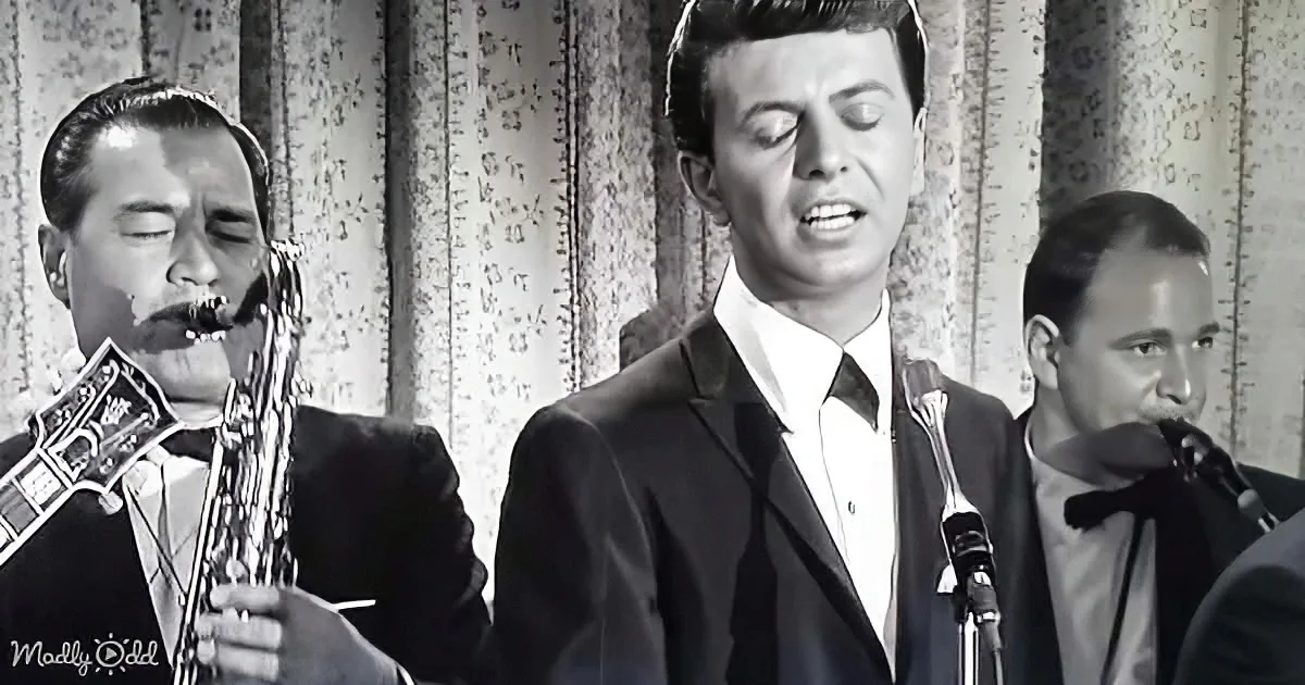 A man in a suit sings into a microphone, accompanied by musicians playing saxophones.