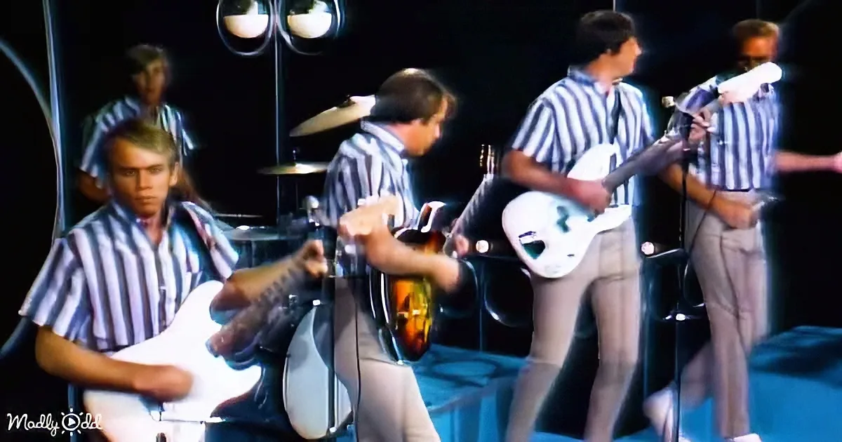 Musicians in striped shirts perform on stage, playing guitars and drums under bright lights.