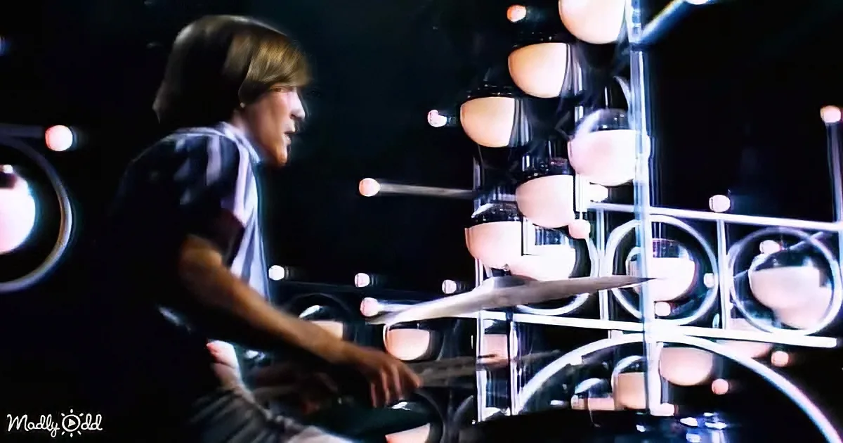 A person plays a unique drum set with multiple circular drums and lights in a dark setting.