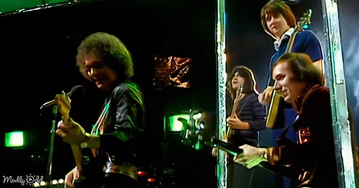 A musician with an afro plays a guitar on stage, illuminated by green lights.