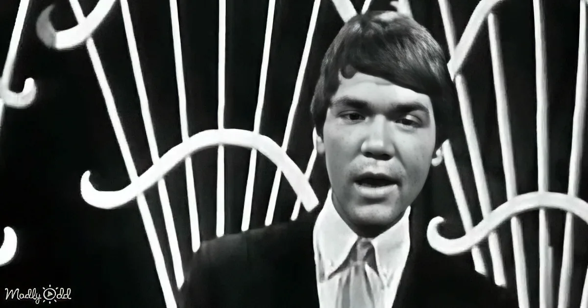 A man in a suit and tie stands in front of a black background with white, abstract patterns.